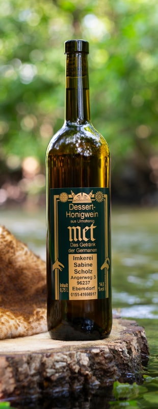 Eine Glasflasche Dessert-Honigwein aus Ulmohonig von Sabine Scholz aus Ebersdorf bei Coburg steht auf einem Baumstumpf am Flussufer.
